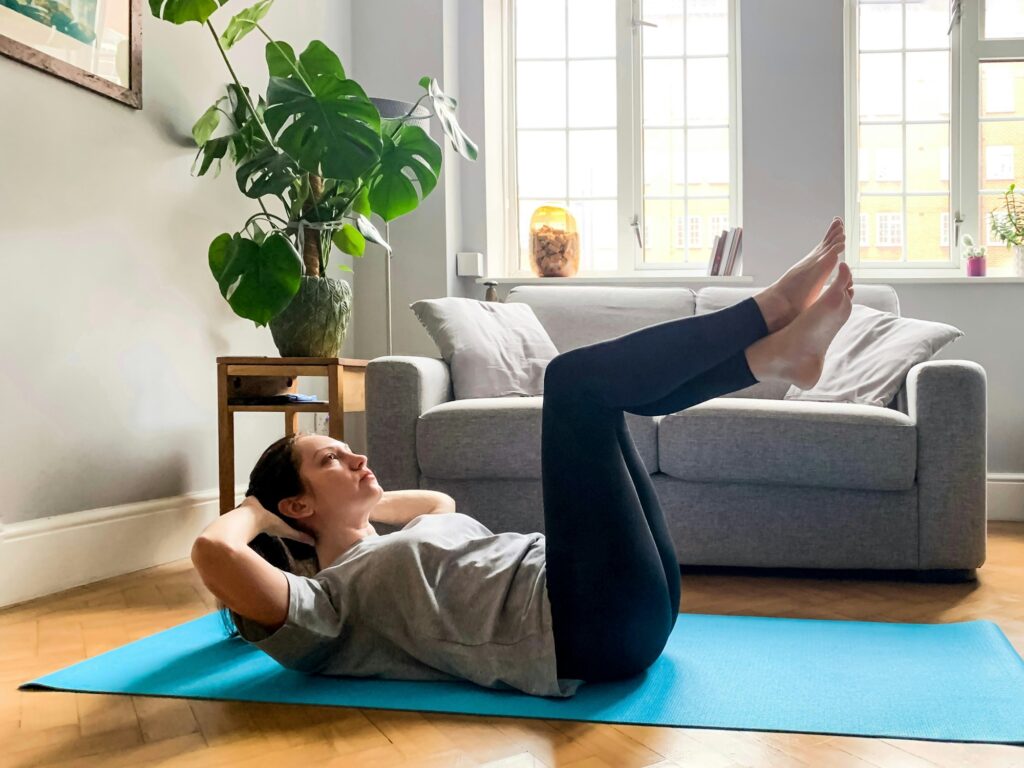 Young woman is doing pilates stretching workout exercises at home on yoga mat. Real people